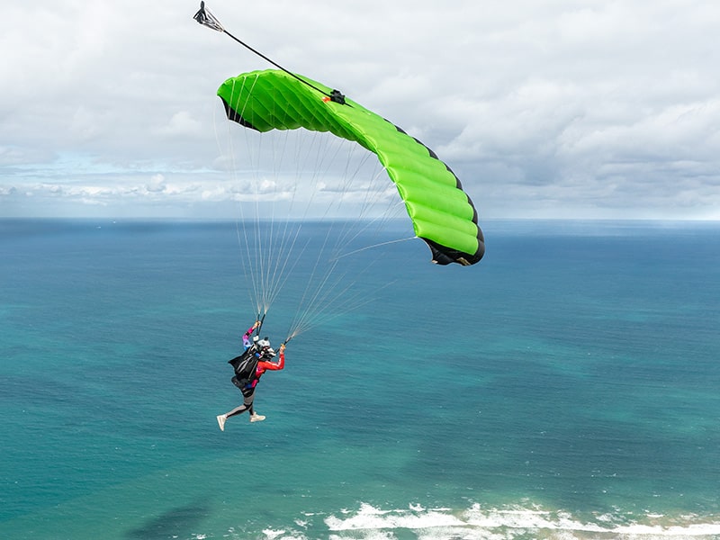 A skydiver with a green parachute, with the water of Torquay in the background.