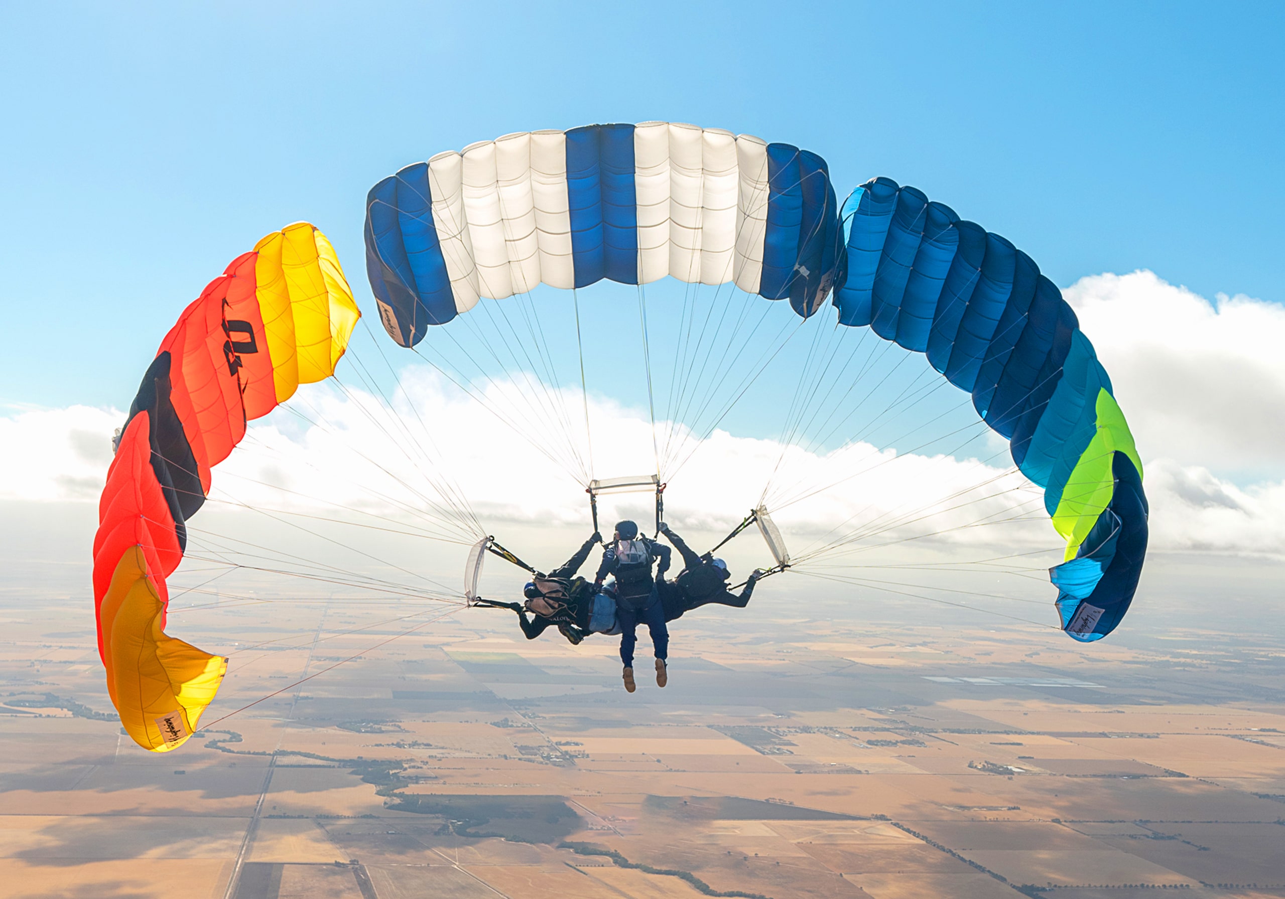 Three friends skydiving in formation with colourful canopies.