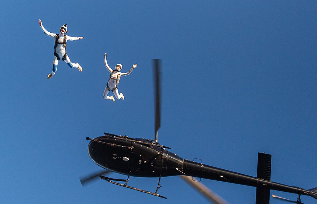 A pair of skydivers jumping out of a helicopter, seen from below.