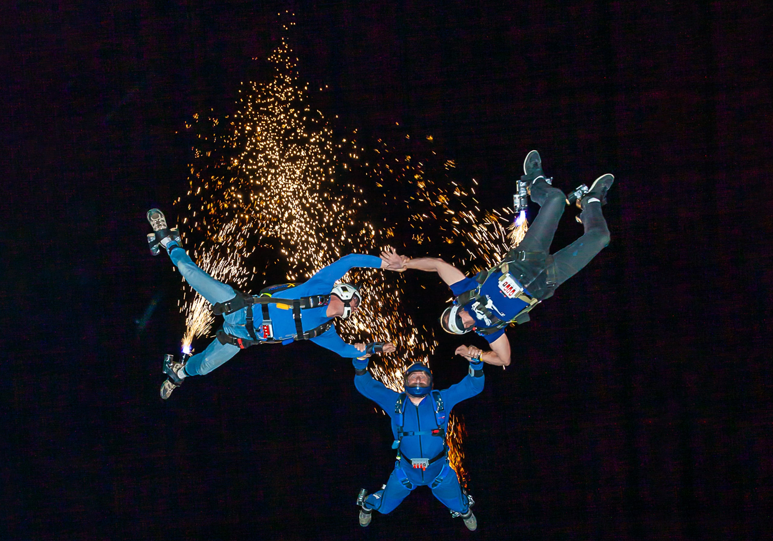 Three skydivers in formation doing a night skydive with fireworks.