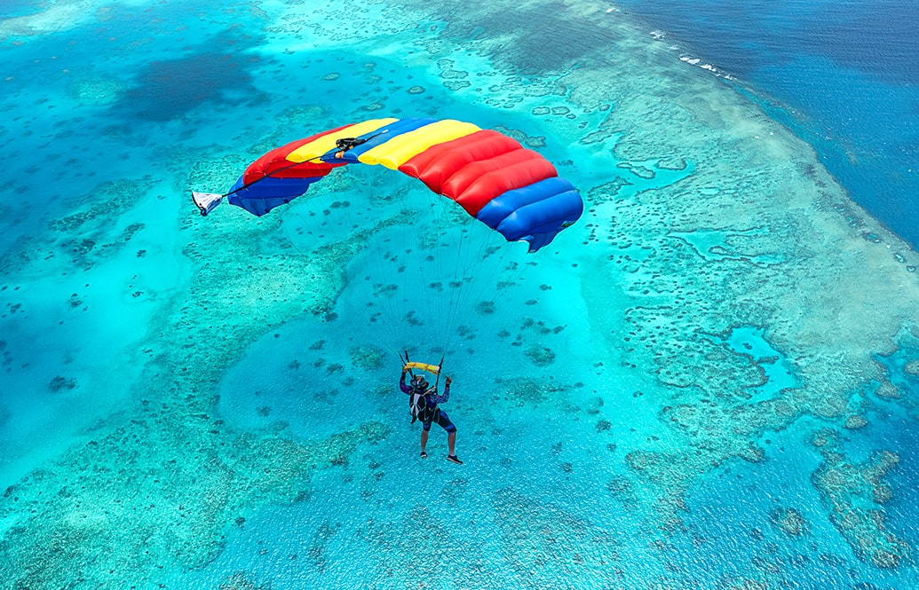 Parachute diving over a reef and blue water in Australia.