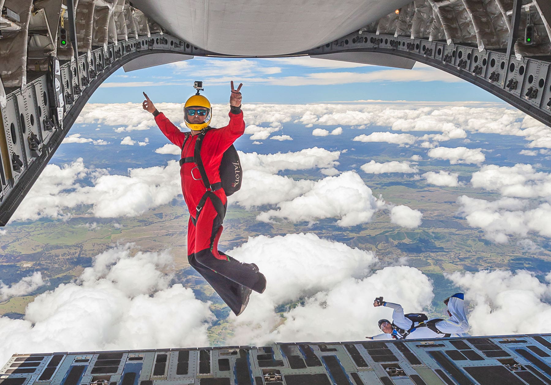 Skydiver in a red flight suit safely jumping out of a military aircraft.