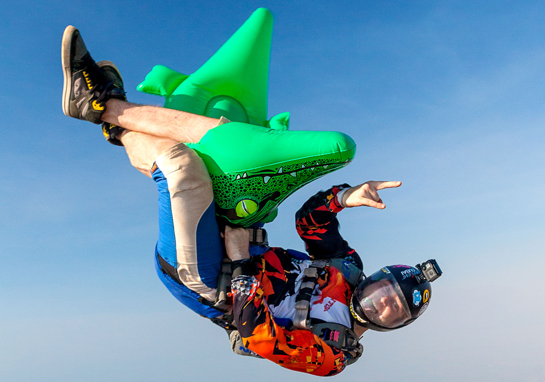 A smiling skydiver in freefall with an inflatable crocodile.